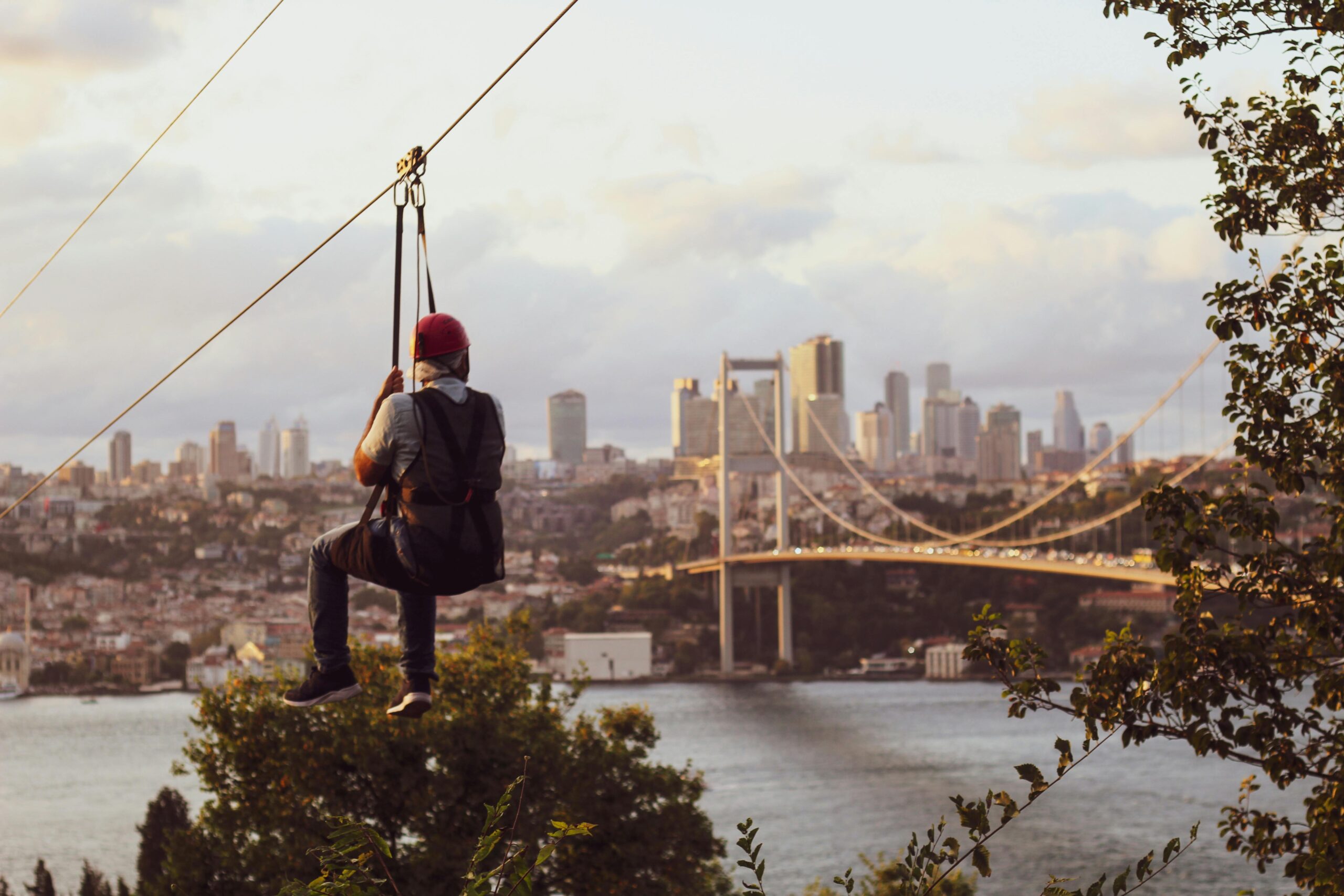 A person ziplining above trees with a stunning view of the Istanbul skyline and Bosphorus Bridge.